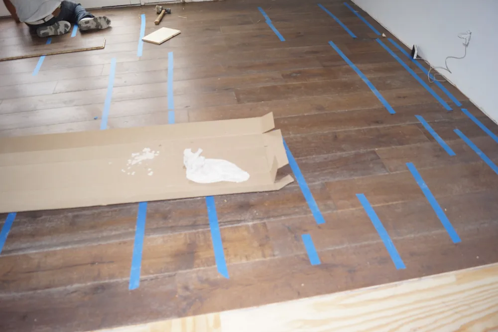 Installed dark wide-plank hardwood floor with temporary blue tape and floor protection in a Pasadena home
