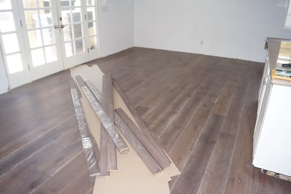 Matching hardwood trim moldings in the same finish laid on cardboard over a finished dark wide-plank floor in Pasadena