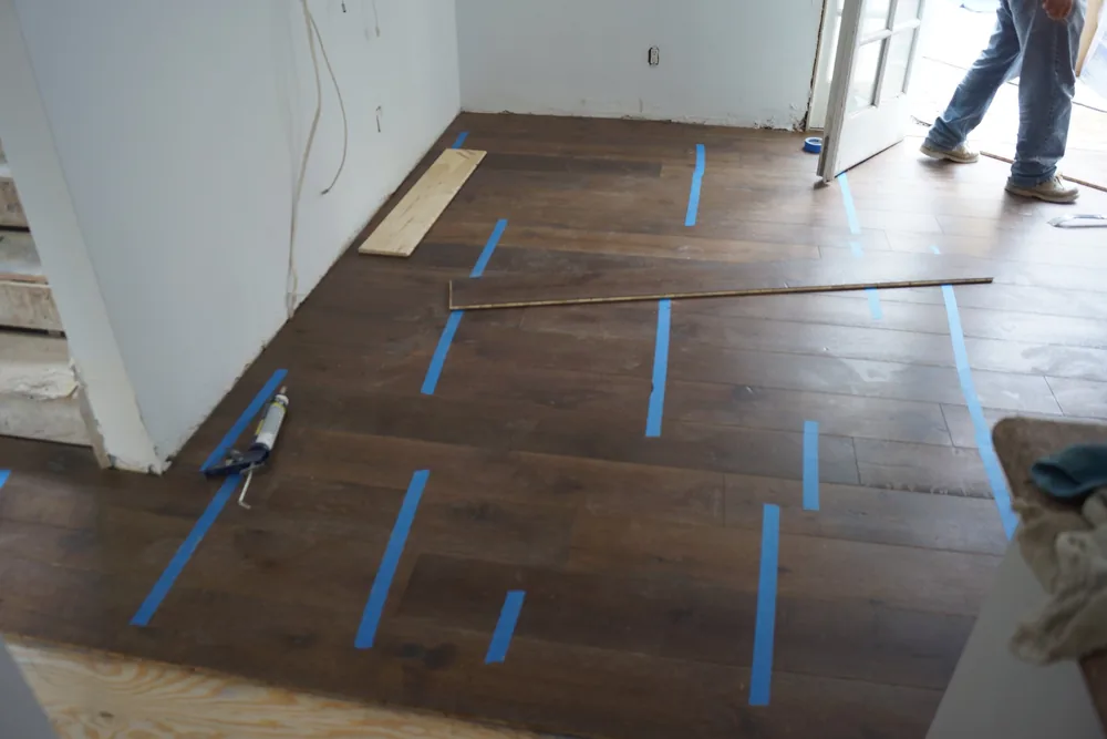 Dark wide-plank hardwood with blue tape across seams and staggered end joints during installation in a Pasadena home