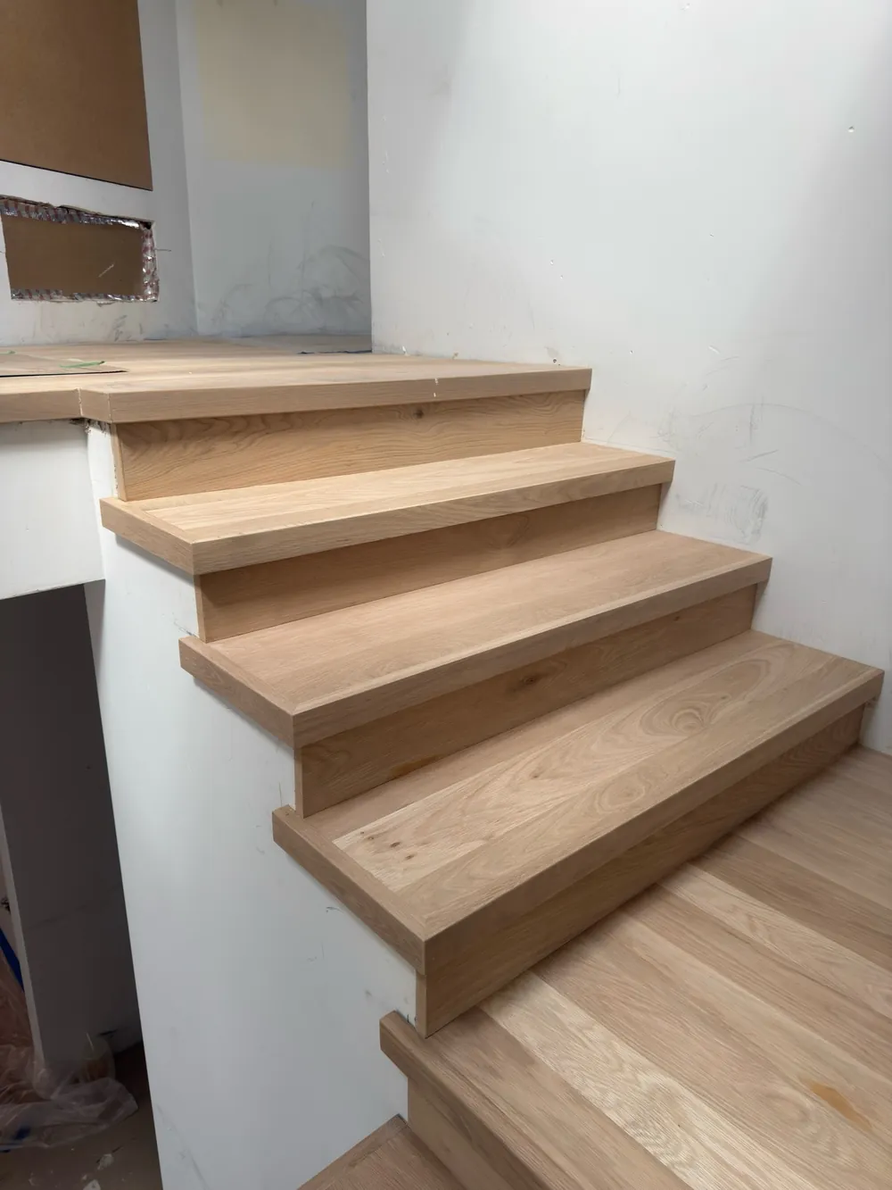 Close view of white oak stair tread ends and wood risers along a side wall, during installation