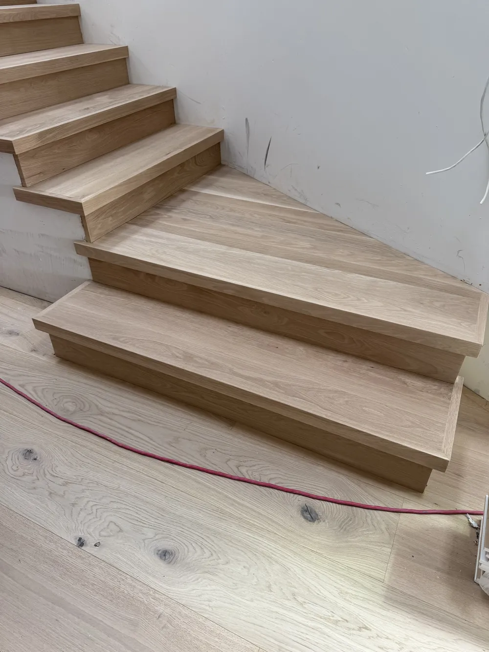 Angled bottom steps of a white oak staircase meeting the hardwood floor, during installation