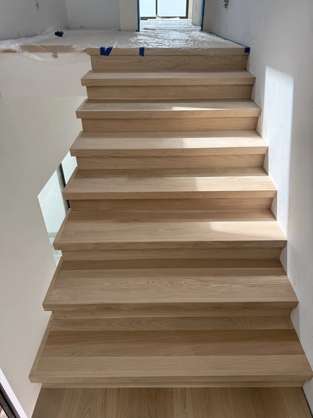 White oak stair treads leading to the upstairs landing, with floor protection still in place