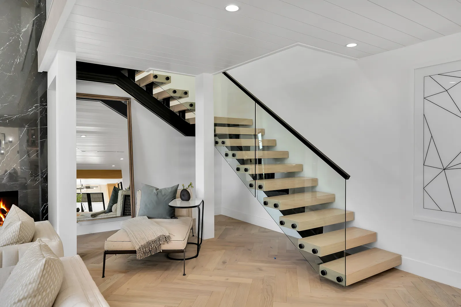 Floating staircase with thick oak treads and glass railing over herringbone floors