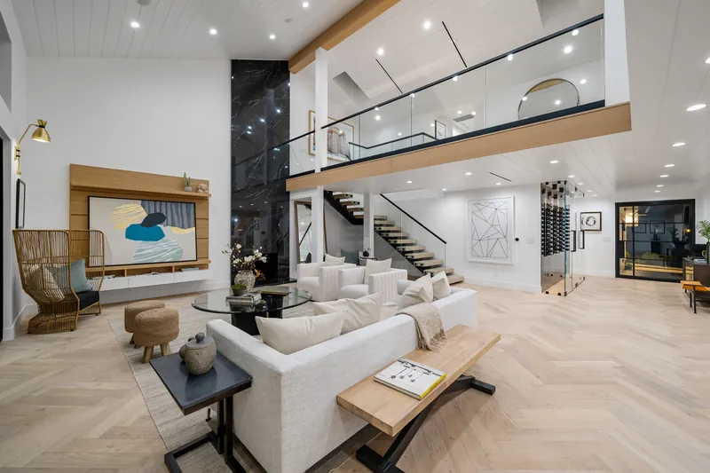 After: the same living room with light herringbone engineered European oak floors, a floor-to-ceiling porcelain slab fireplace, floating oak stairs and a glass-railed loft