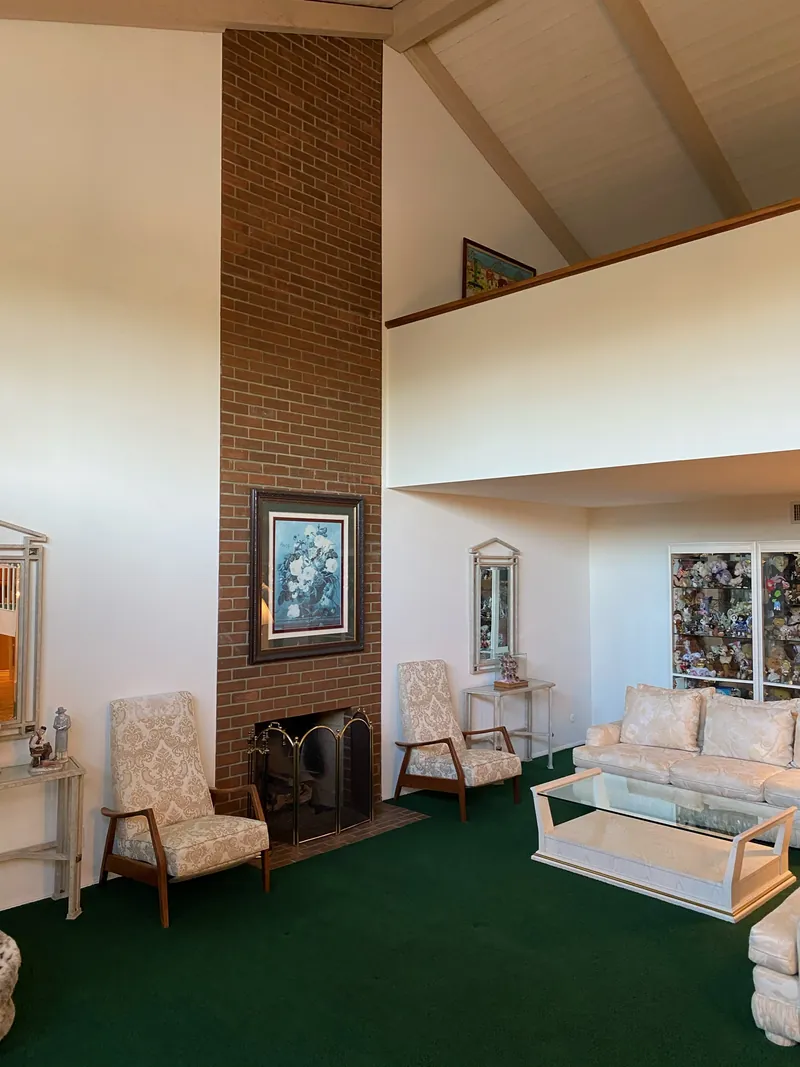 Before: two-story living room with dark green carpet, a brick chimney fireplace and a solid loft wall