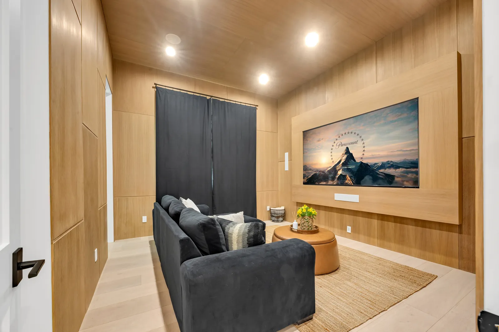 Media room with oak-paneled walls and ceiling over wide-plank light oak hardwood floors